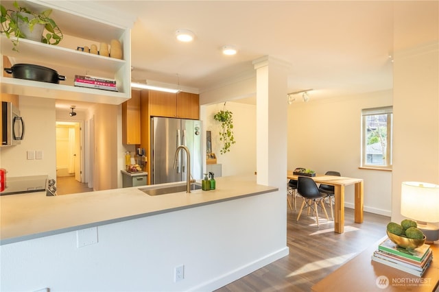 kitchen featuring freestanding refrigerator, a sink, wood finished floors, a peninsula, and brown cabinetry