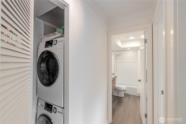 clothes washing area with stacked washer and clothes dryer, wood finished floors, and crown molding