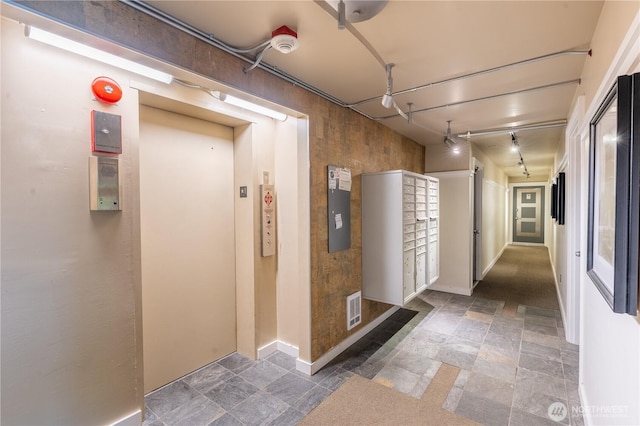 hall with stone tile flooring, baseboards, and elevator