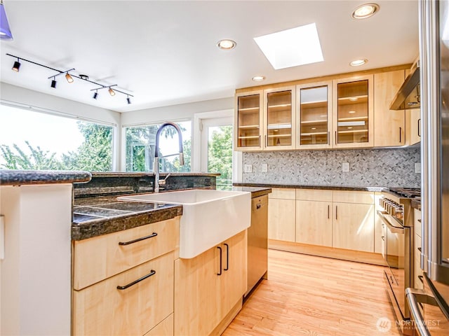4441 53rd Ave SW, Seattle, WA 98116 - kitchen featuring light brown cabinets, a skylight, appliances with stainless steel finishes, dark countertops, and backsplash