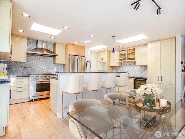 4441 53rd Ave SW, Seattle, WA 98116 - kitchen featuring wall chimney range hood, appliances with stainless steel finishes, light brown cabinets, a skylight, and recessed lighting