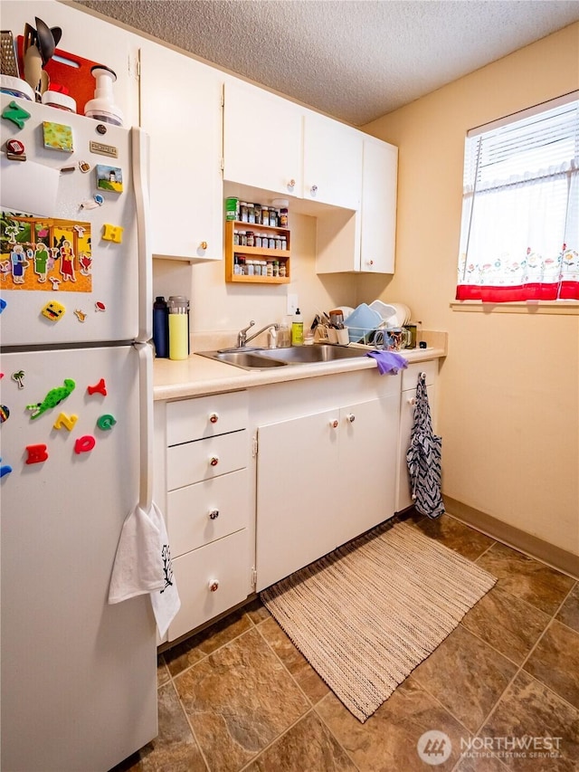 kitchen with freestanding refrigerator, a sink, light countertops, white cabinets, and a textured ceiling