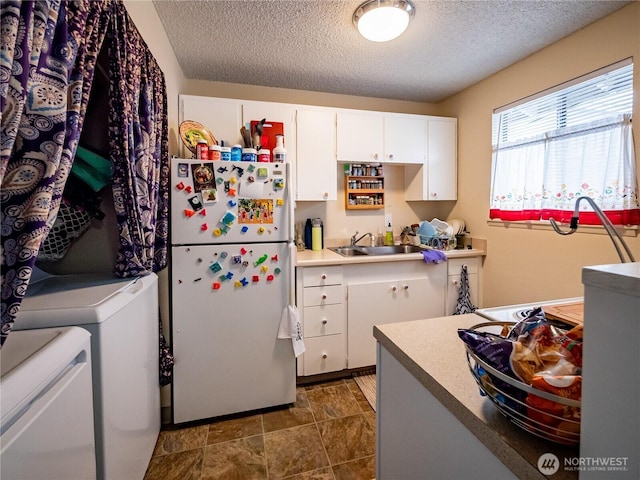 kitchen featuring freestanding refrigerator, a sink, independent washer and dryer, a textured ceiling, and white cabinetry