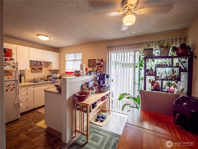 kitchen with freestanding refrigerator, a sink, white cabinetry, light countertops, and ceiling fan