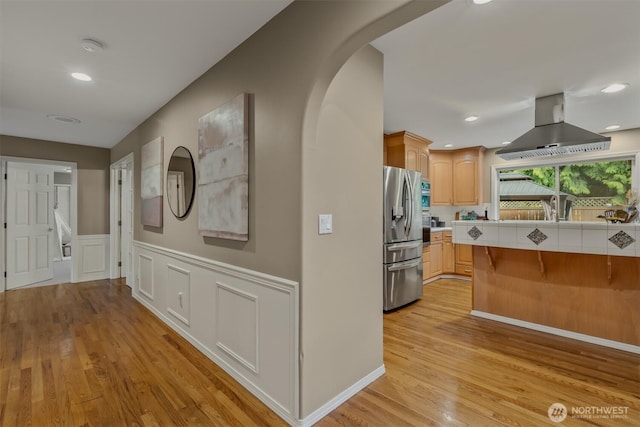 hallway featuring arched walkways, light wood-style flooring, a wainscoted wall, recessed lighting, and a decorative wall