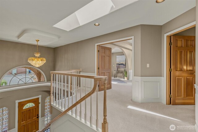 hall with a chandelier, an upstairs landing, arched walkways, carpet flooring, and a skylight
