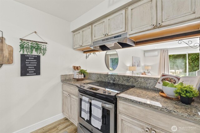 kitchen with electric stove, under cabinet range hood, baseboards, light wood-style floors, and a wall mounted air conditioner