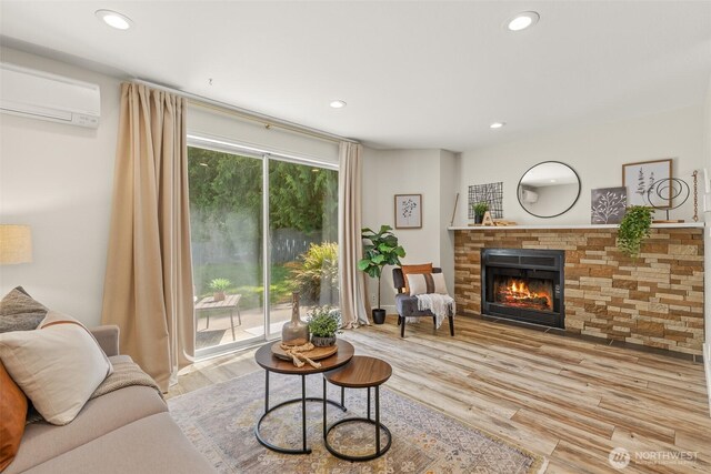 living room with an AC wall unit, a glass covered fireplace, recessed lighting, and wood finished floors