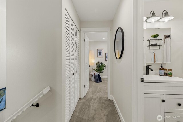 hallway with a sink, light colored carpet, and baseboards