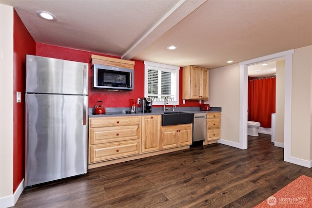 kitchen featuring appliances with stainless steel finishes, dark countertops, dark wood-style floors, a sink, and light brown cabinetry