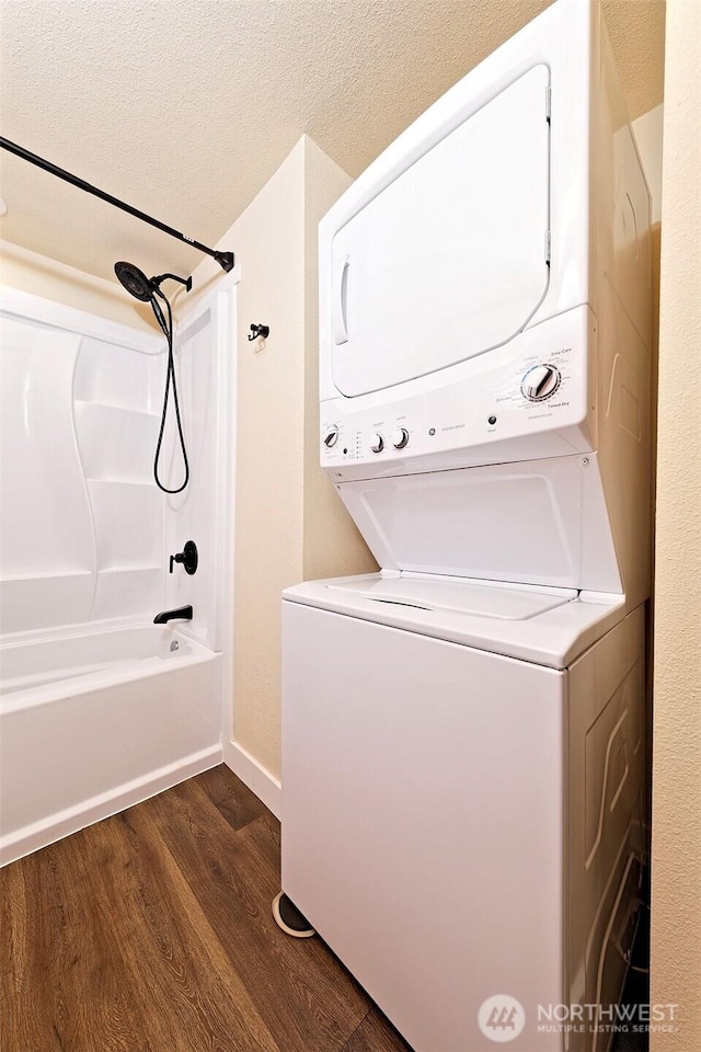 washroom featuring stacked washer / dryer, dark wood finished floors, baseboards, and a textured ceiling