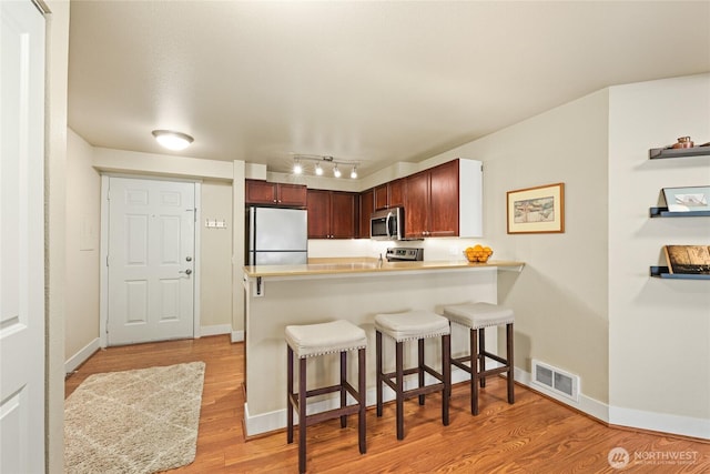 kitchen featuring stainless steel appliances, light wood finished floors, a kitchen bar, and light countertops