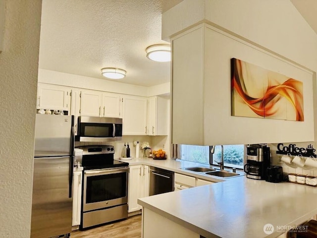 kitchen with appliances with stainless steel finishes, a sink, a peninsula, light countertops, and white cabinets