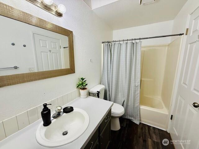 bathroom featuring toilet, vanity, wood finished floors, and shower / bath combination with curtain