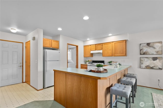 236 W Maberry Dr Unit 102, Lynden, WA 98264 - kitchen with white appliances, a peninsula, under cabinet range hood, light colored carpet, and a breakfast bar area