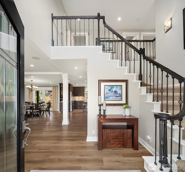 stairway with a high ceiling, wood finished floors, ornate columns, a chandelier, and baseboards