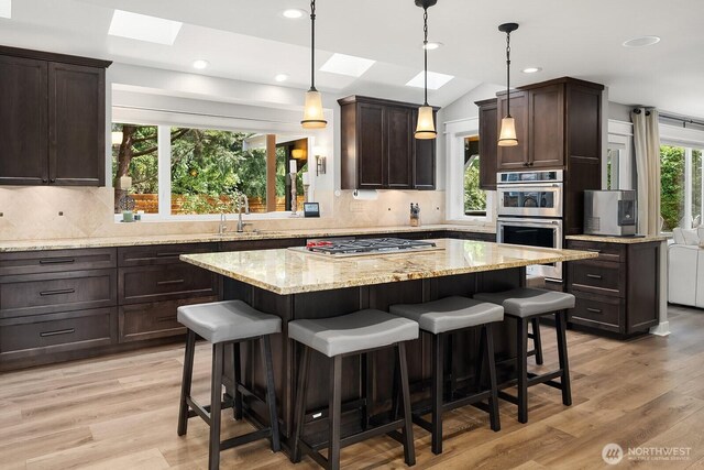 kitchen featuring a skylight, appliances with stainless steel finishes, a sink, dark brown cabinets, and a center island
