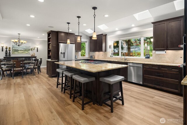 kitchen with stainless steel appliances, dark brown cabinetry, a skylight, tasteful backsplash, and a kitchen island