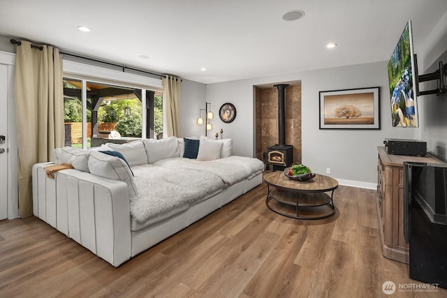 living room with wood finished floors, a wood stove, baseboards, and recessed lighting