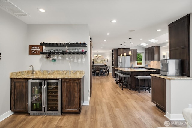 indoor bar featuring wine cooler, stainless steel fridge, light wood finished floors, baseboards, and pendant lighting