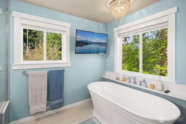 full bath with plenty of natural light, a freestanding bath, a chandelier, and tile patterned flooring