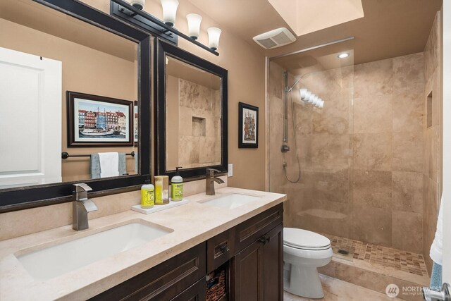 full bathroom featuring a tile shower, toilet, and double vanity