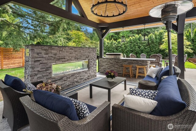view of patio / terrace with an outdoor living space with a fireplace, exterior bar, and fence