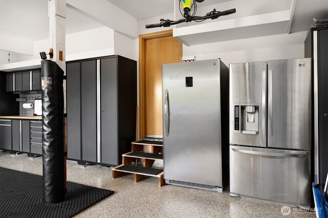 kitchen with stainless steel refrigerator with ice dispenser, freestanding refrigerator, and dark speckled floor