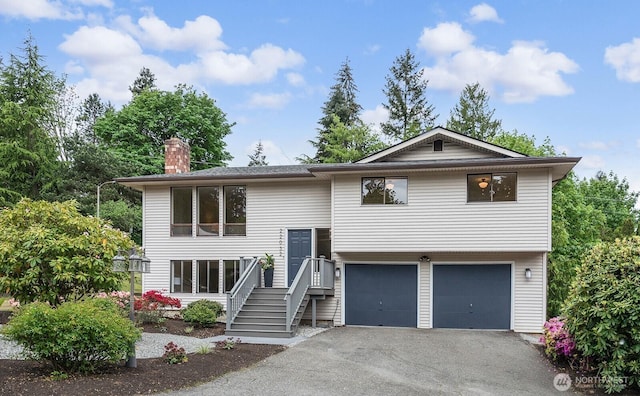 bi-level home with an attached garage, driveway, and a chimney