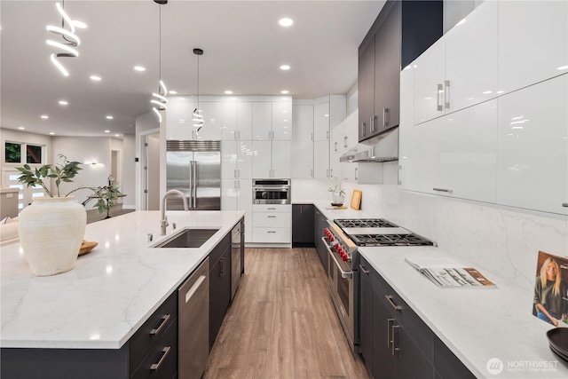 kitchen featuring high end appliances, modern cabinets, under cabinet range hood, a sink, and white cabinetry