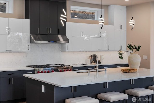kitchen featuring under cabinet range hood, a sink, a breakfast bar area, and dark cabinetry