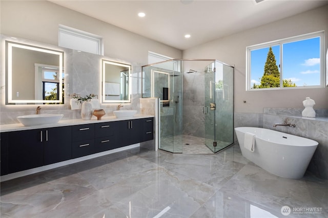 bathroom with tile walls, marble tiled floors, a freestanding bath, a stall shower, and double vanity
