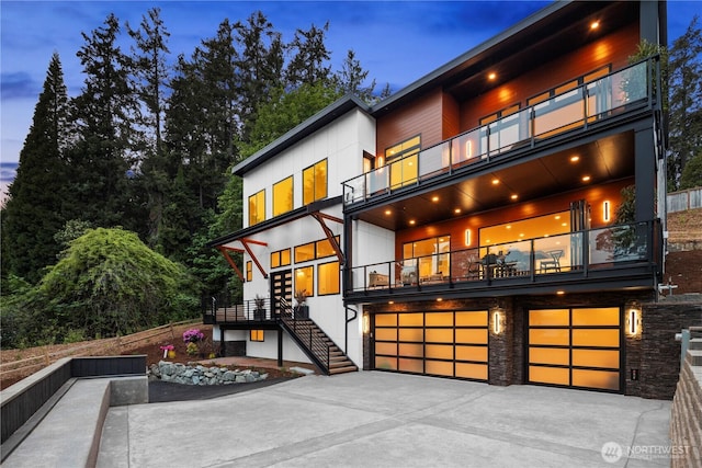 back of house with a balcony, stairway, an attached garage, and concrete driveway