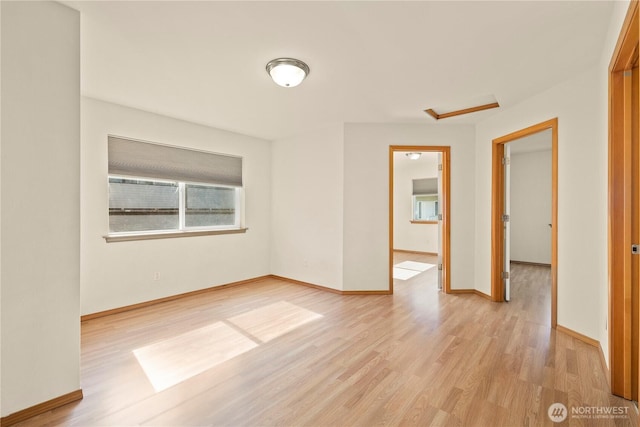 spare room featuring light wood-type flooring, attic access, and baseboards