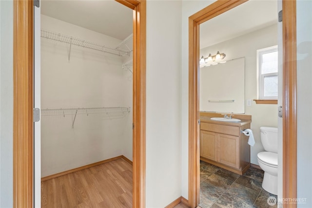 bathroom with toilet, vanity, baseboards, and a walk in closet