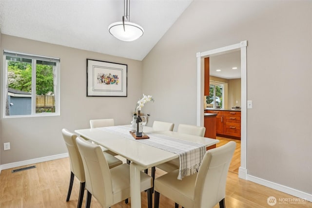 dining area with vaulted ceiling, baseboards, and light wood finished floors