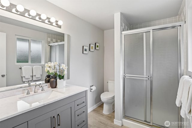 bathroom with a shower stall, toilet, vanity, and wood finished floors