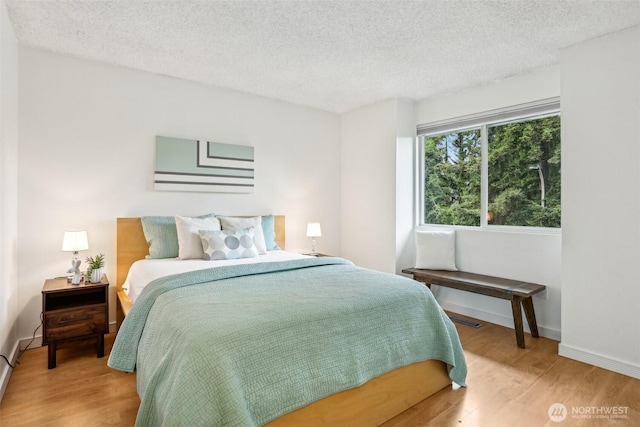 bedroom with a textured ceiling, light wood-style floors, and baseboards