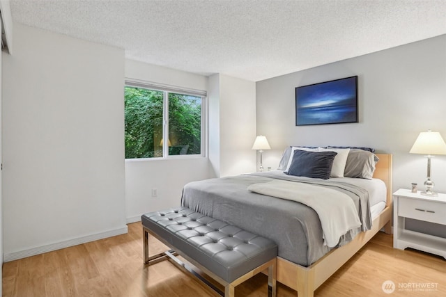 bedroom featuring a textured ceiling, light wood finished floors, and baseboards