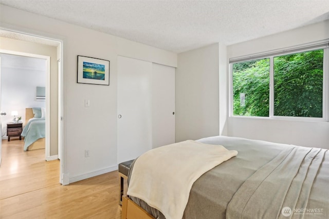bedroom with light wood finished floors, a textured ceiling, a closet, and baseboards