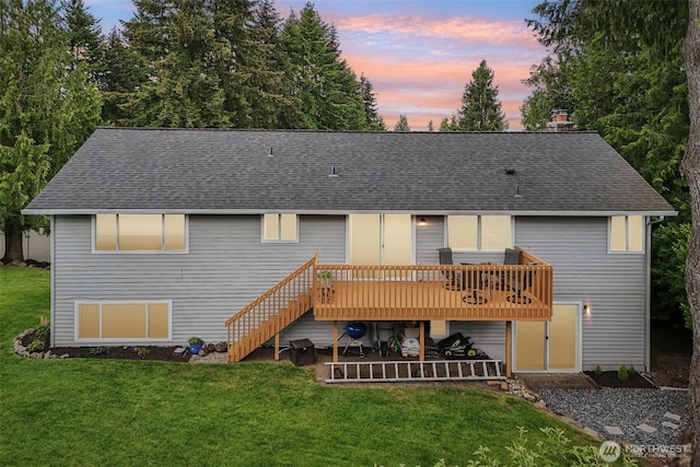 back of house at dusk featuring a shingled roof, a wooden deck, stairs, and a lawn