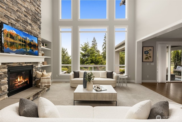 living area with a towering ceiling, a stone fireplace, and baseboards