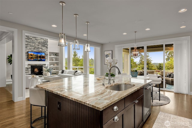 kitchen with a sink, dark brown cabinetry, wood finished floors, recessed lighting, and a stone fireplace