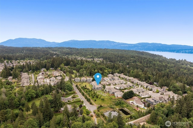 view of property location with a forest, nearby suburban area, and a water and mountain view