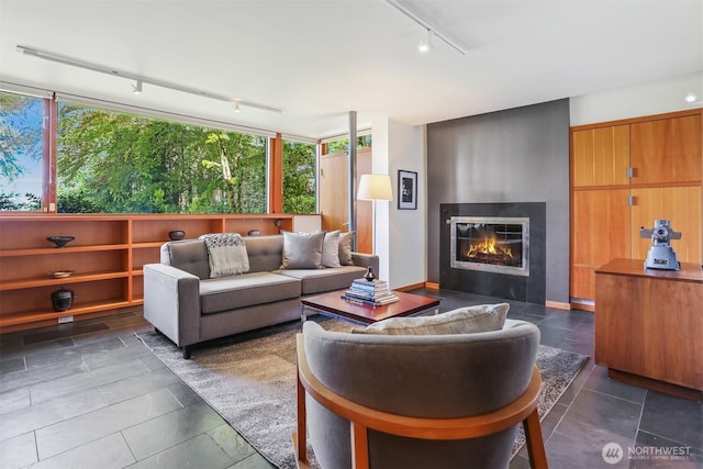 living room featuring rail lighting, a glass covered fireplace, and dark tile patterned flooring