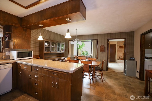 kitchen with white appliances, wallpapered walls, a peninsula, light countertops, and glass insert cabinets