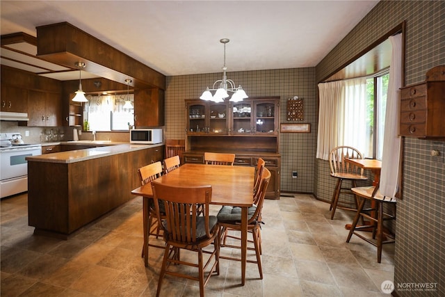 dining room featuring wallpapered walls, plenty of natural light, a chandelier, and stone finish floors