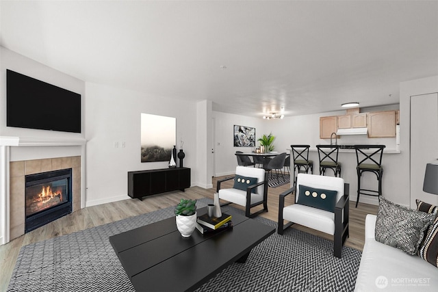 living room featuring light wood finished floors, a tile fireplace, and baseboards