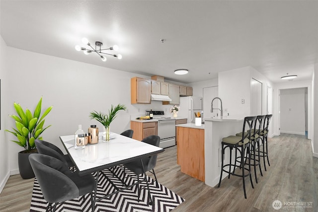 kitchen with white appliances, under cabinet range hood, light wood-style floors, light countertops, and a breakfast bar area