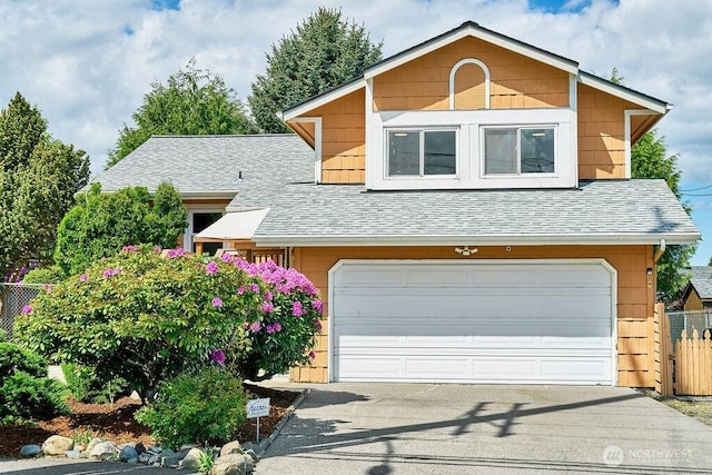 view of front of house with roof with shingles, fence, an attached garage, and driveway